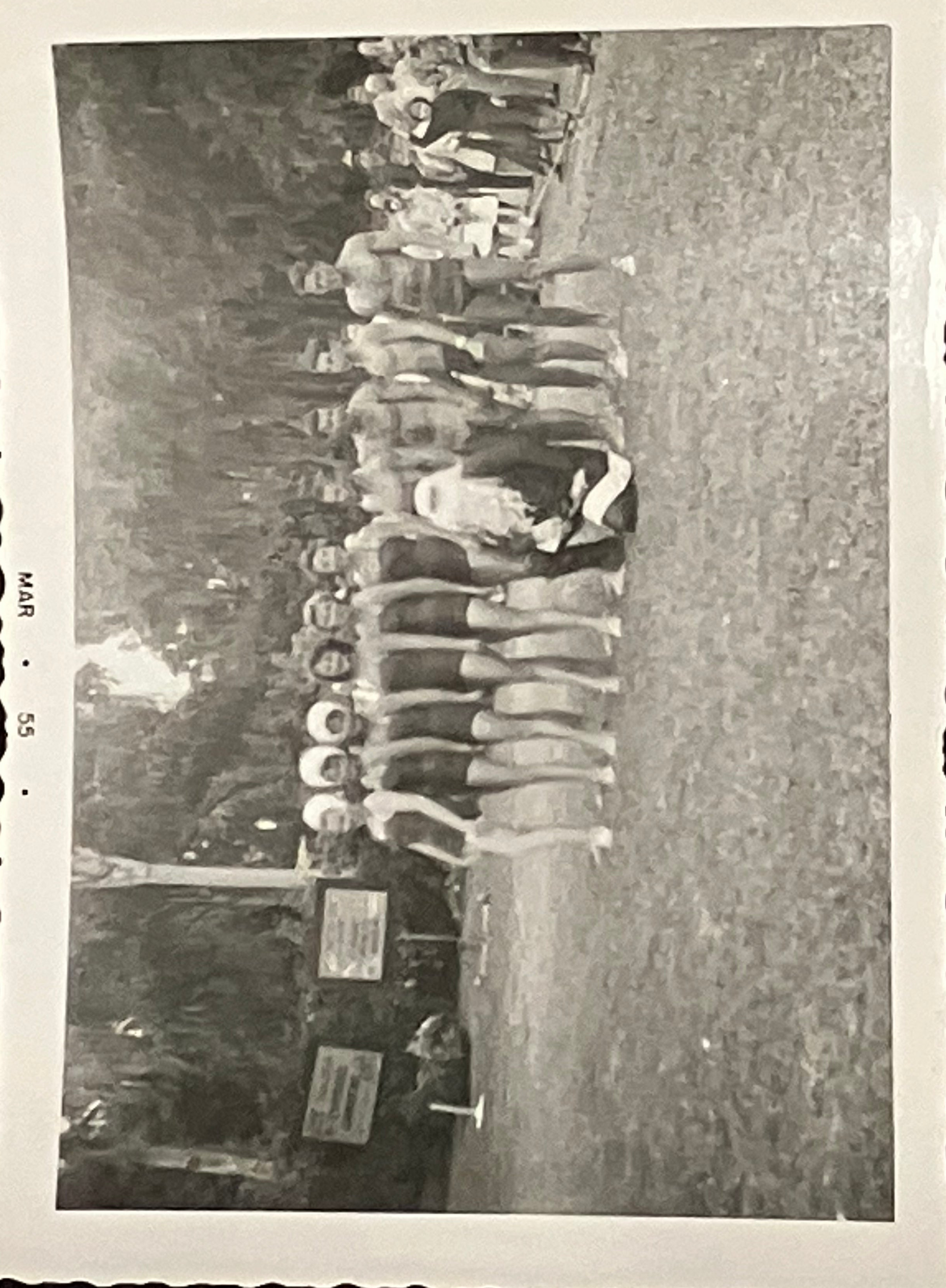 Vintage black and white photo of a line of people in bathing suits standing on a grassy field.