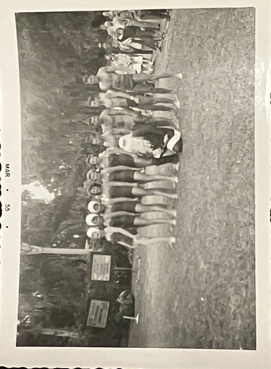 Vintage black and white photo of a line of people in bathing suits standing on a grassy field.