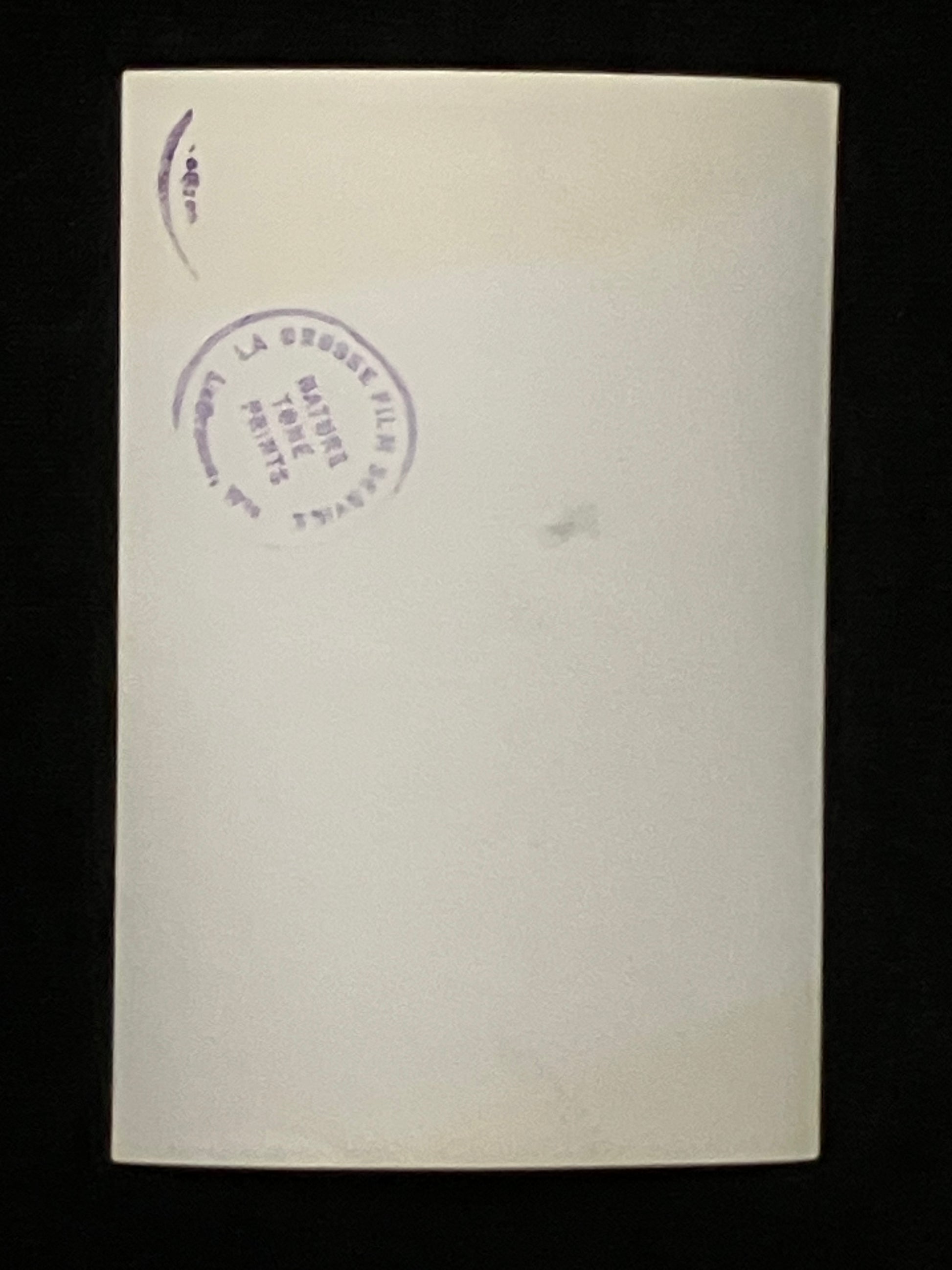 A blank cream-colored photo back with a purple circular stamp on the upper left, displayed against a solid black background.