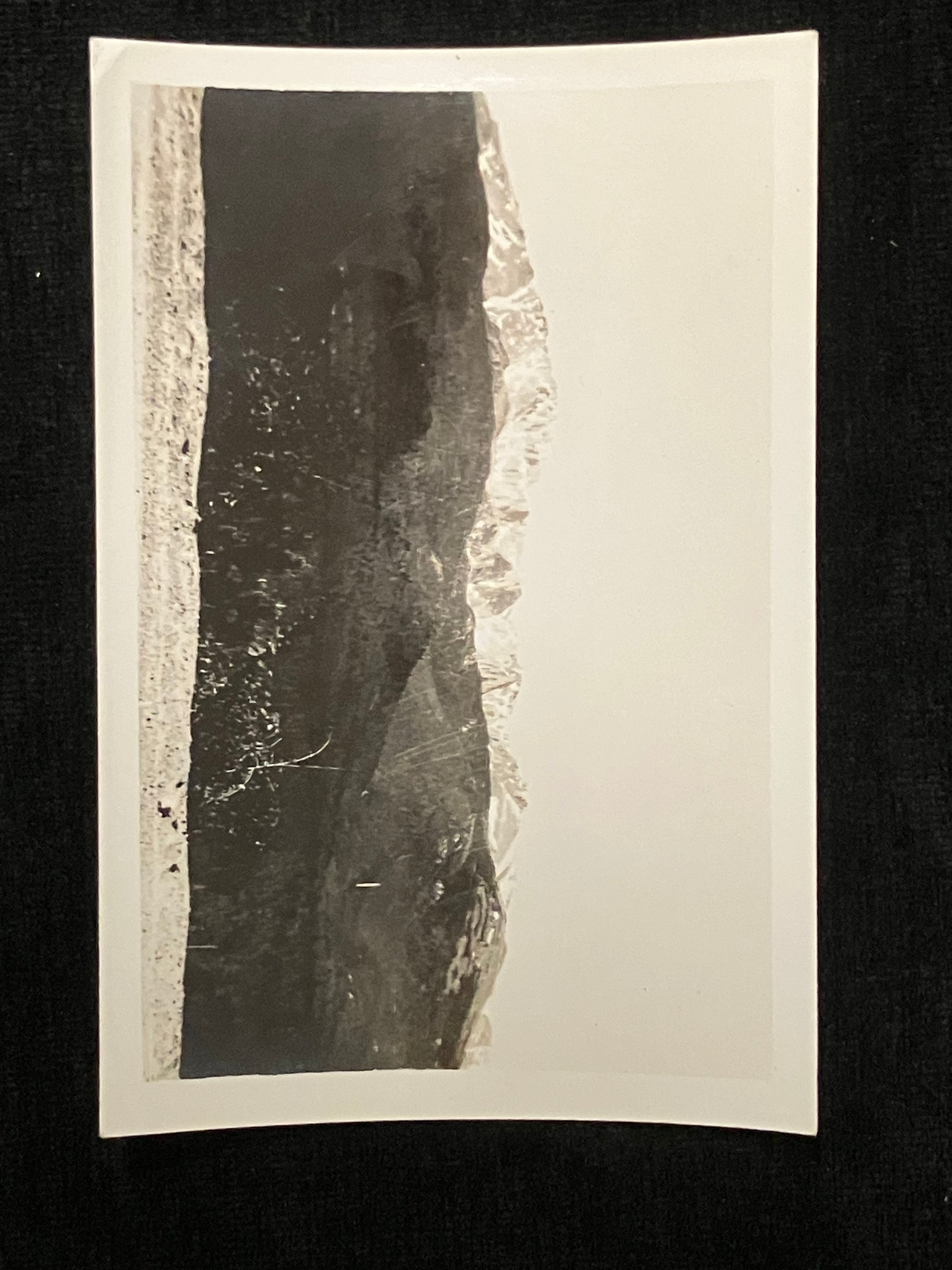 A black and white photographic print mounted with a white paper border, displayed against a dark black background.