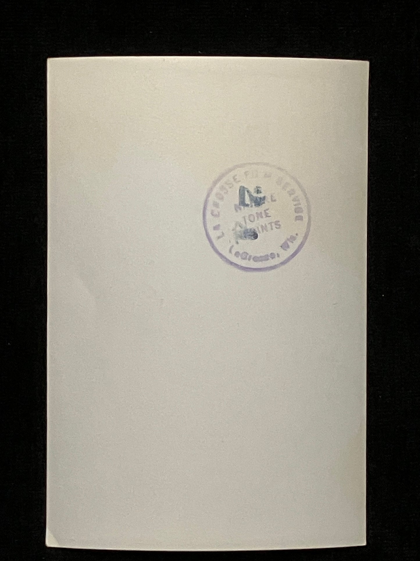 A cream-colored paper photo with a circular purple stamp in the center, set against a solid black background.