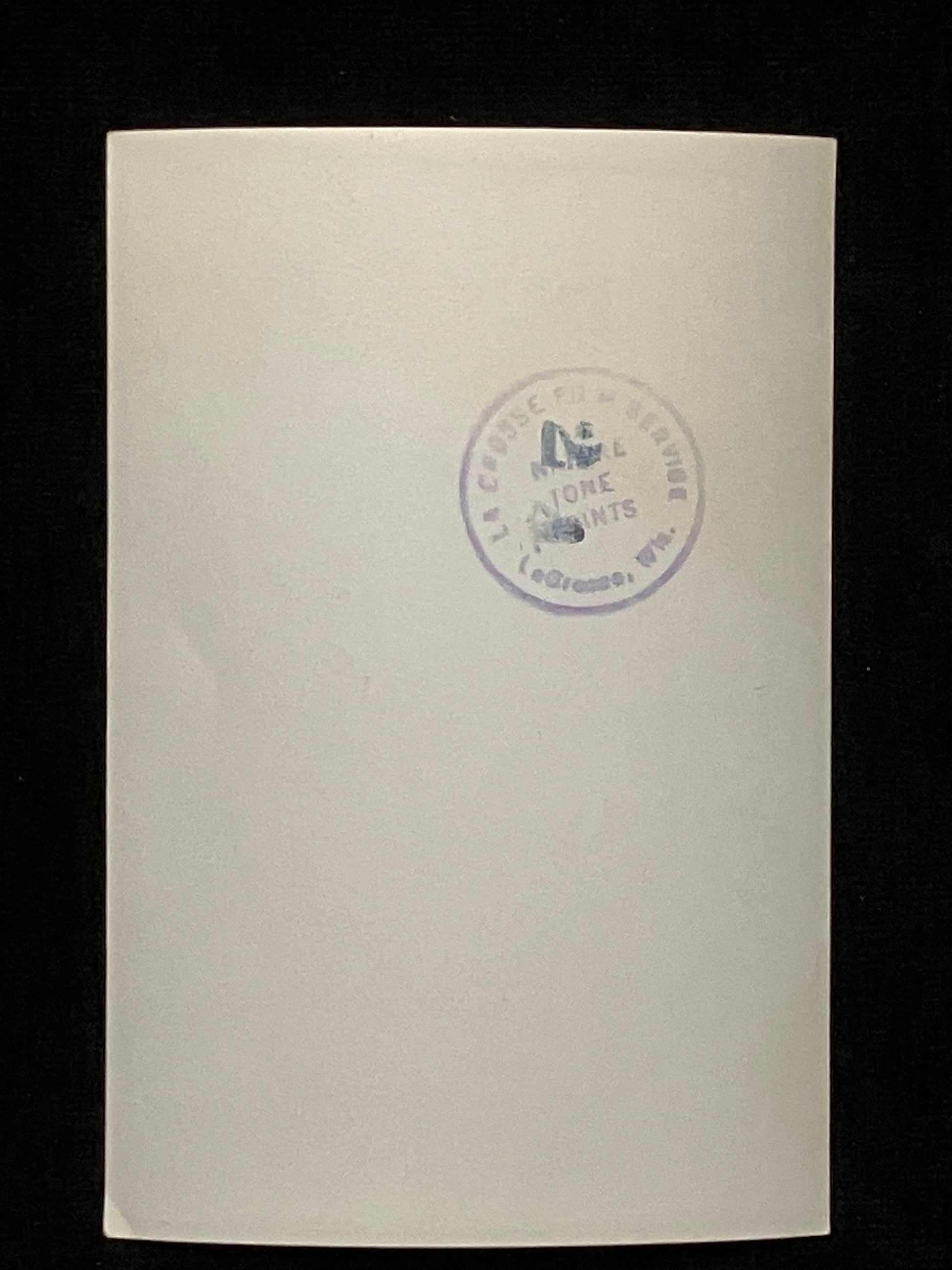 A cream-colored paper photo with a circular purple stamp in the center, set against a solid black background.