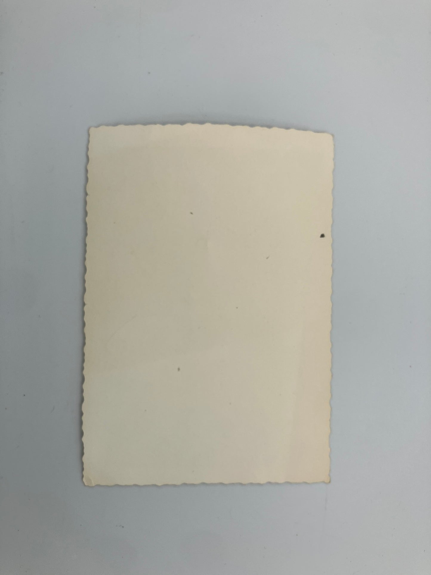 A blank, aged cream-colored paper card with scalloped edges, lying flat on a light gray background.
