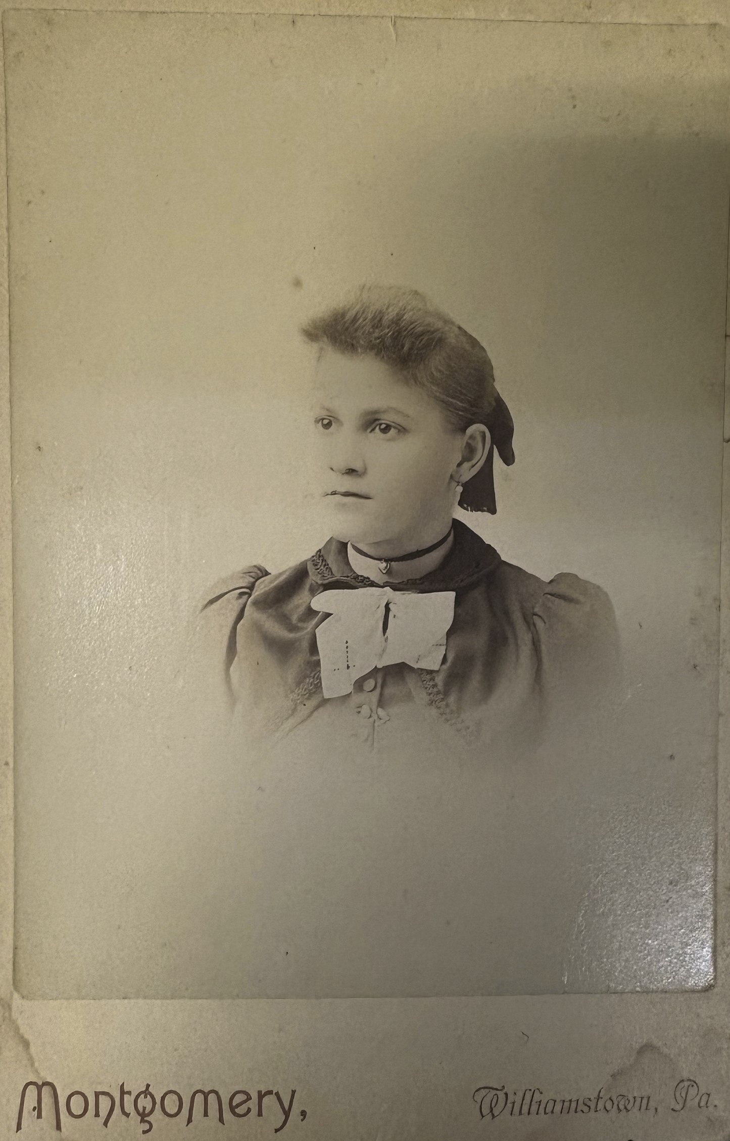 Vintage sepia-toned portrait of a young girl with a bow, likely from the late 19th century.