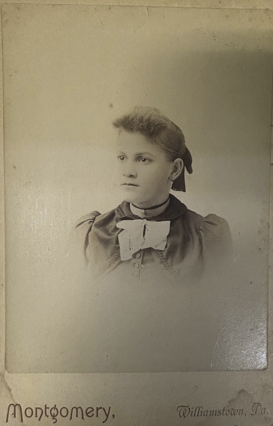 Vintage sepia-toned portrait of a young girl with a bow, likely from the late 19th century.