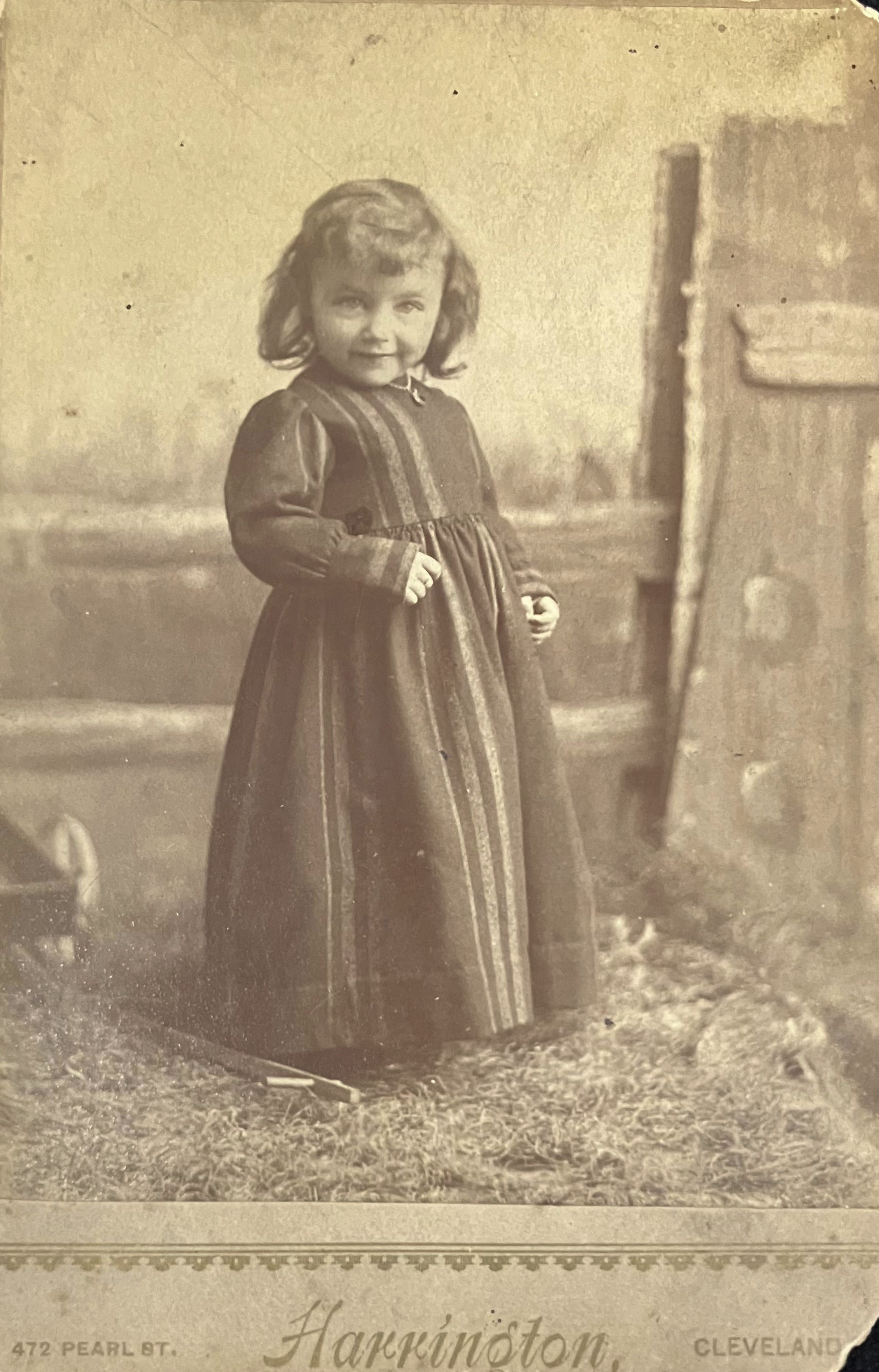Vintage sepia-toned photograph of a young girl in a dress standing outdoors.