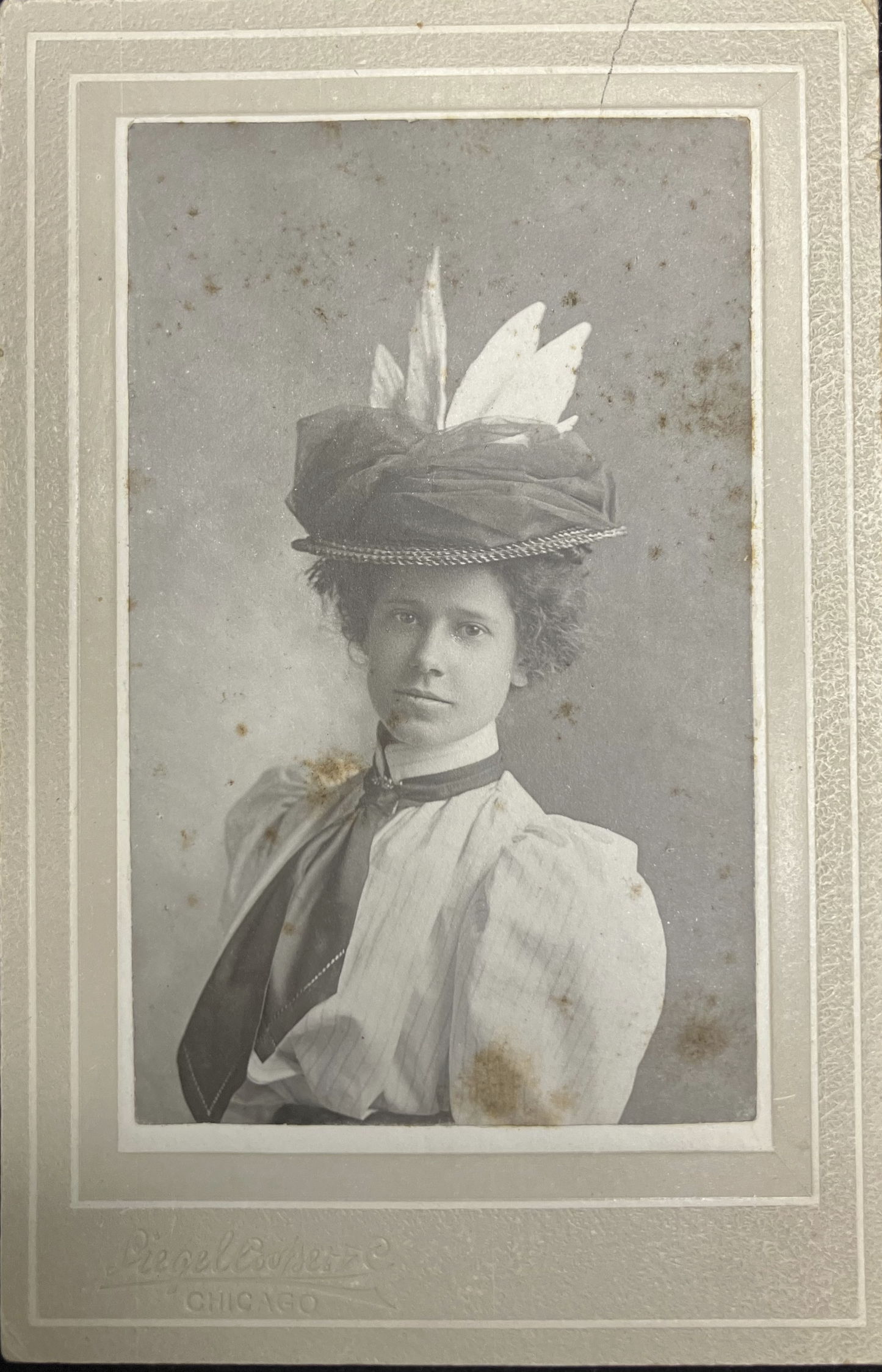 Vintage photograph of a woman wearing an ornate hat with feathers on a dark background