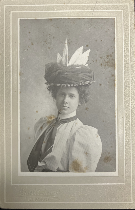 Vintage photograph of a woman wearing an ornate hat with feathers on a dark background