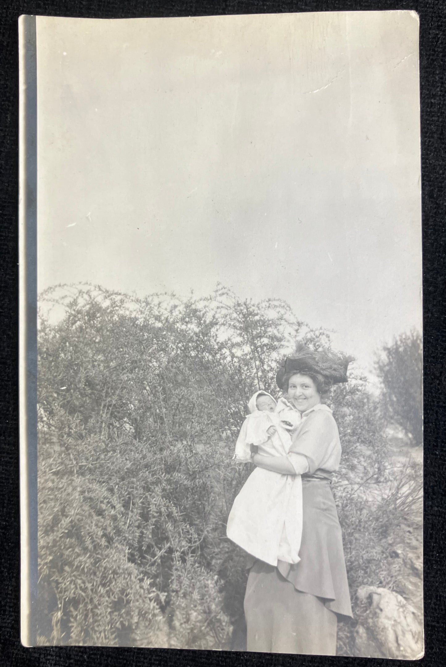 Vintage black and white photo of a woman holding a child outdoors with trees in the background