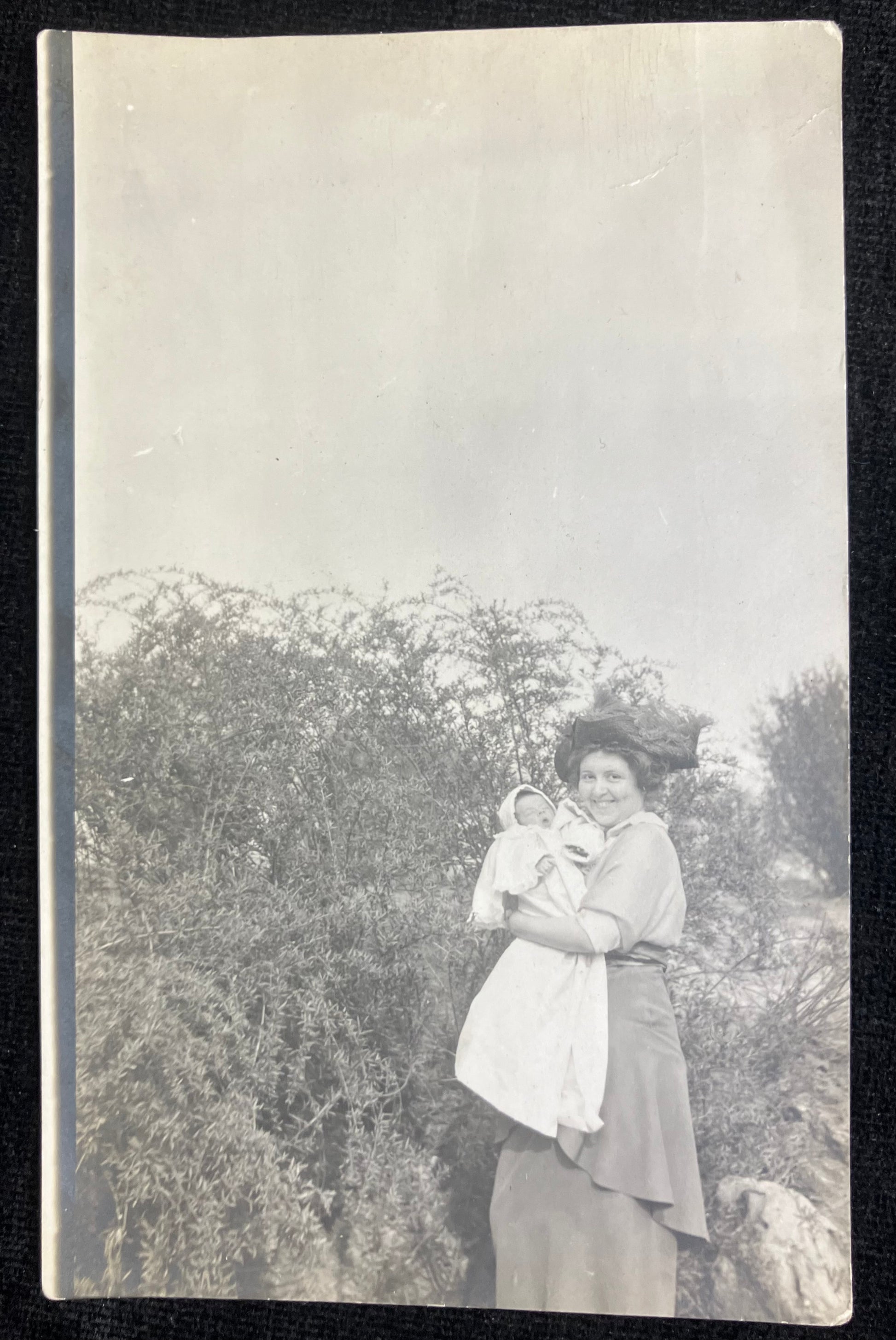 Vintage black and white photo of a woman holding a child outdoors with trees in the background