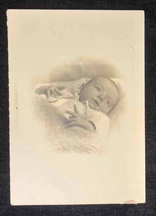 Vintage sepia-toned photograph of a baby lying on a surface with a blurred background