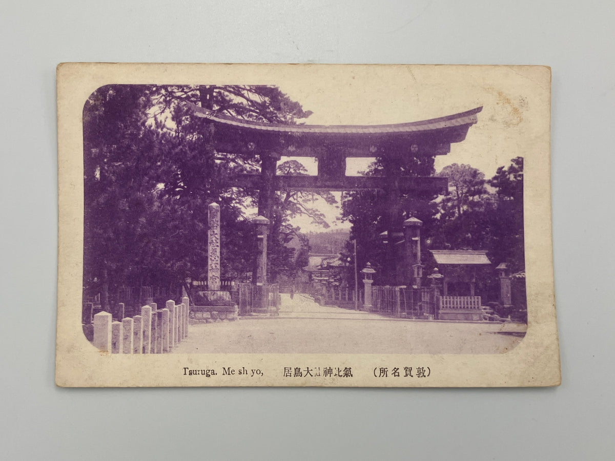 A vintage Japanese postcard showing a temple gate in Japan, printed in a sepia-toned monochrome style with Japanese text along the bottom, displayed against a neutral light gray background.