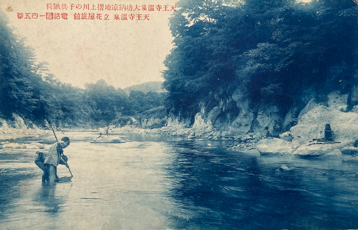 A vintage Japanese postcard depicting a scenic river with a figure wading in the water, shown against a neutral light gray background.