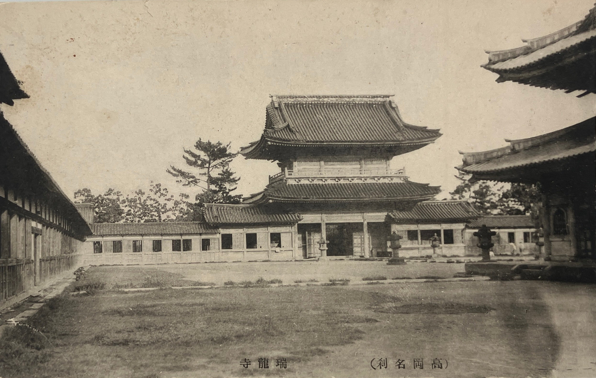 A vintage sepia-toned postcard depicting a traditional Japanese courtyard with a central pagoda-style building, shown against a light gray background.
