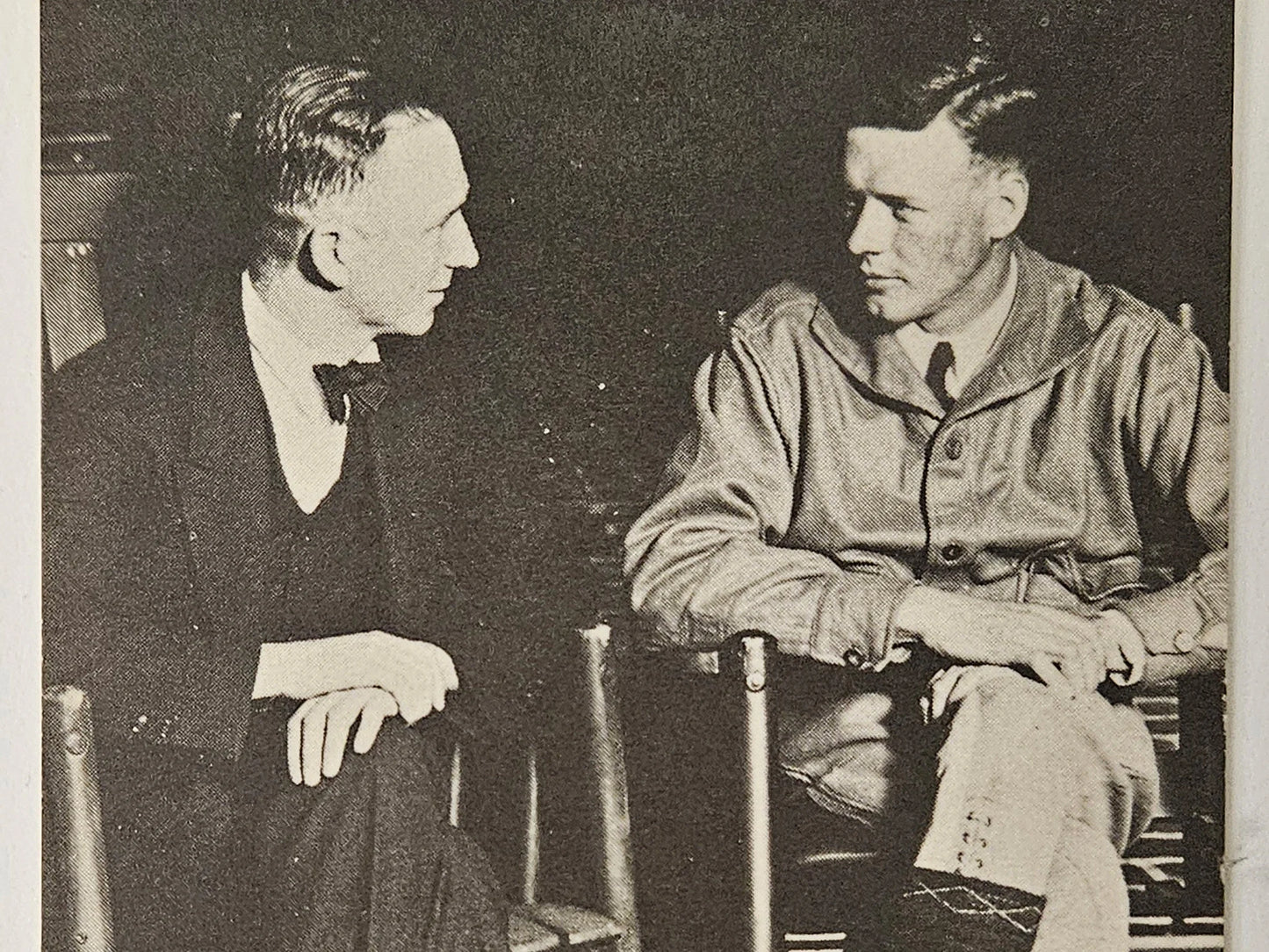 Two men sitting in chairs, one in formal attire and the other in a military uniform, engaged in conversation.