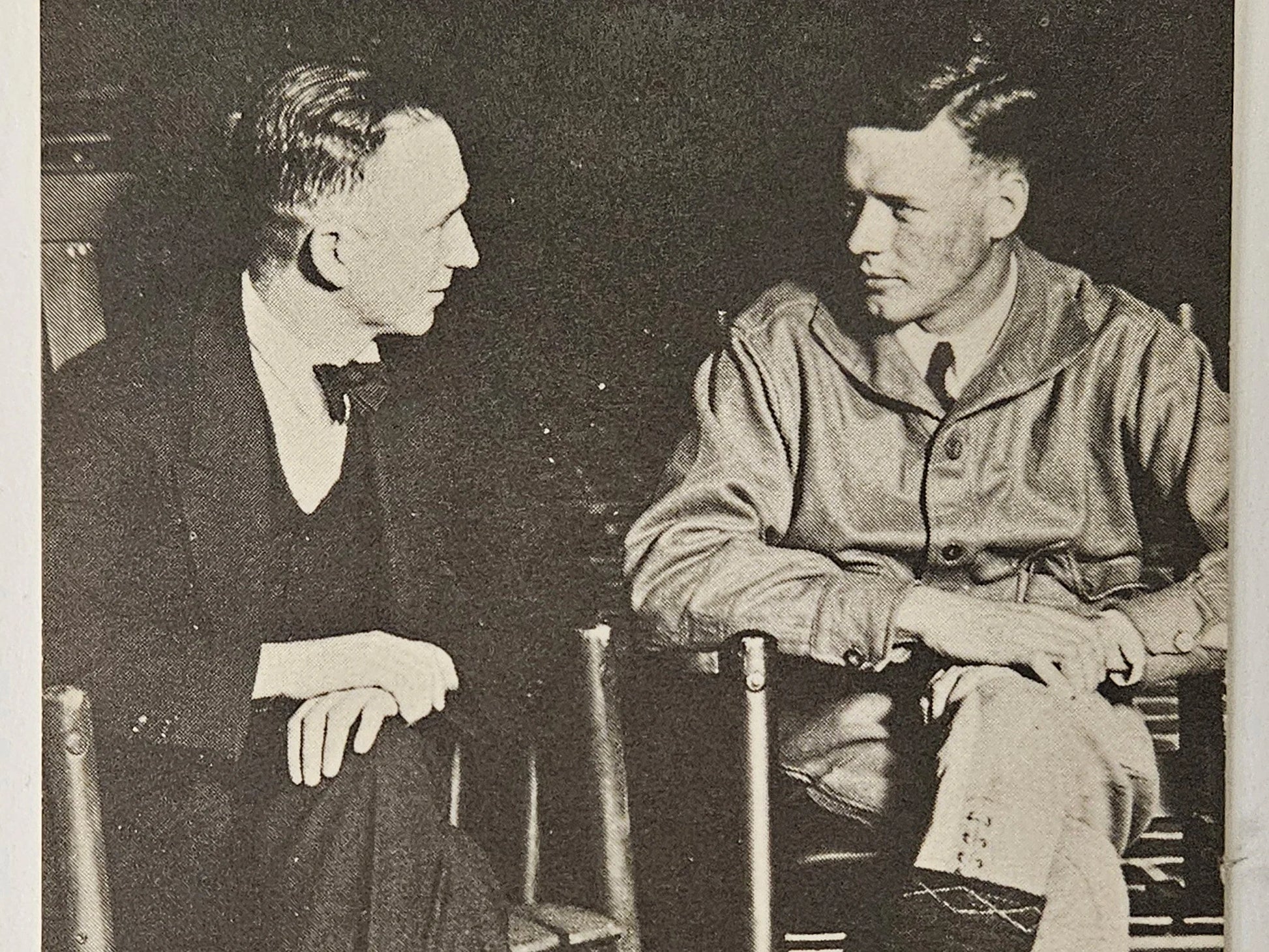 Two men sitting in chairs, one in formal attire and the other in a military uniform, engaged in conversation.