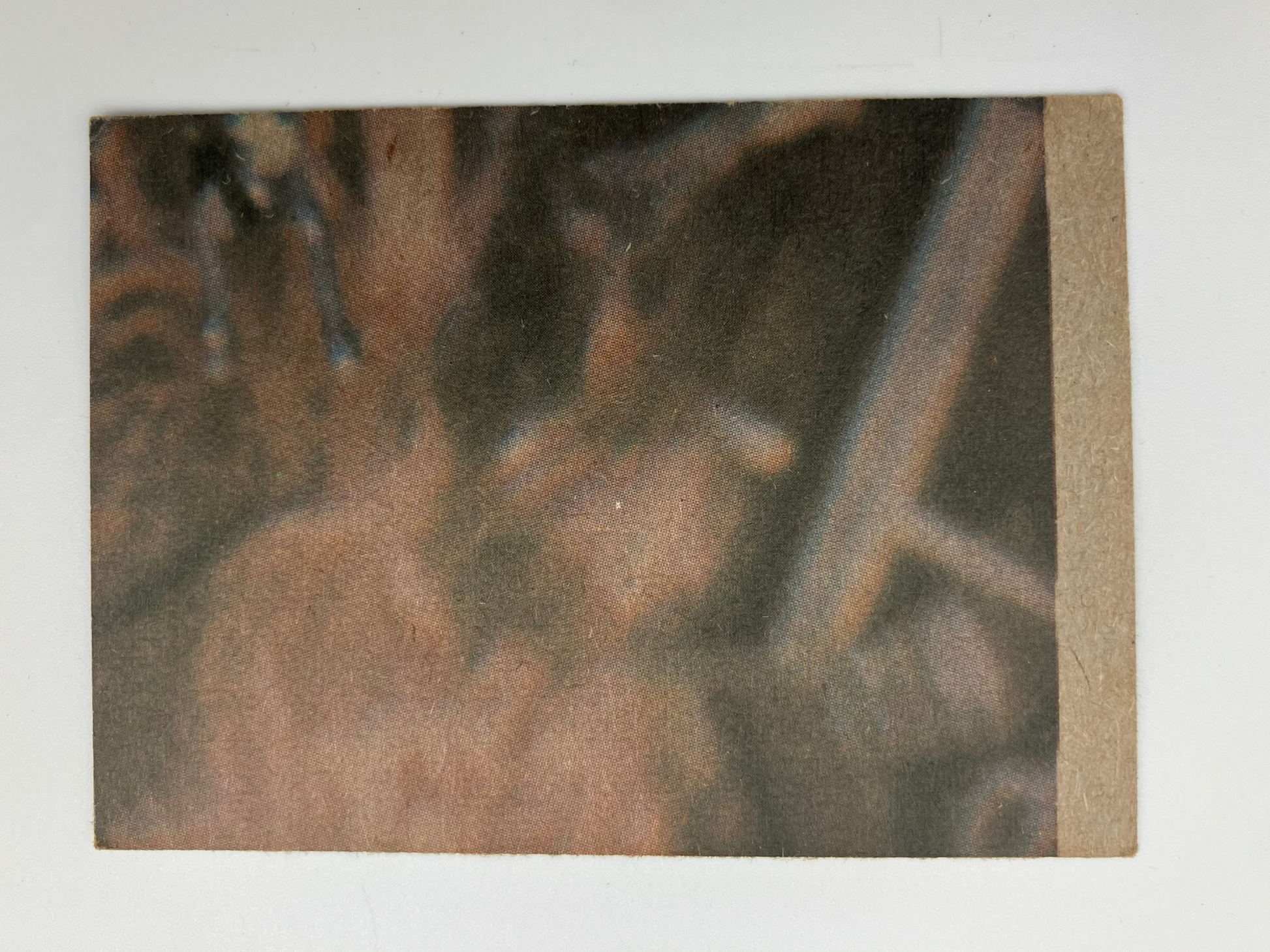 A square art print or photograph mounted on a light gray background, featuring an abstract close-up scene in earthy tones of brown, tan, and dark gray. The print has a textured surface and a tan strip along the top edge.