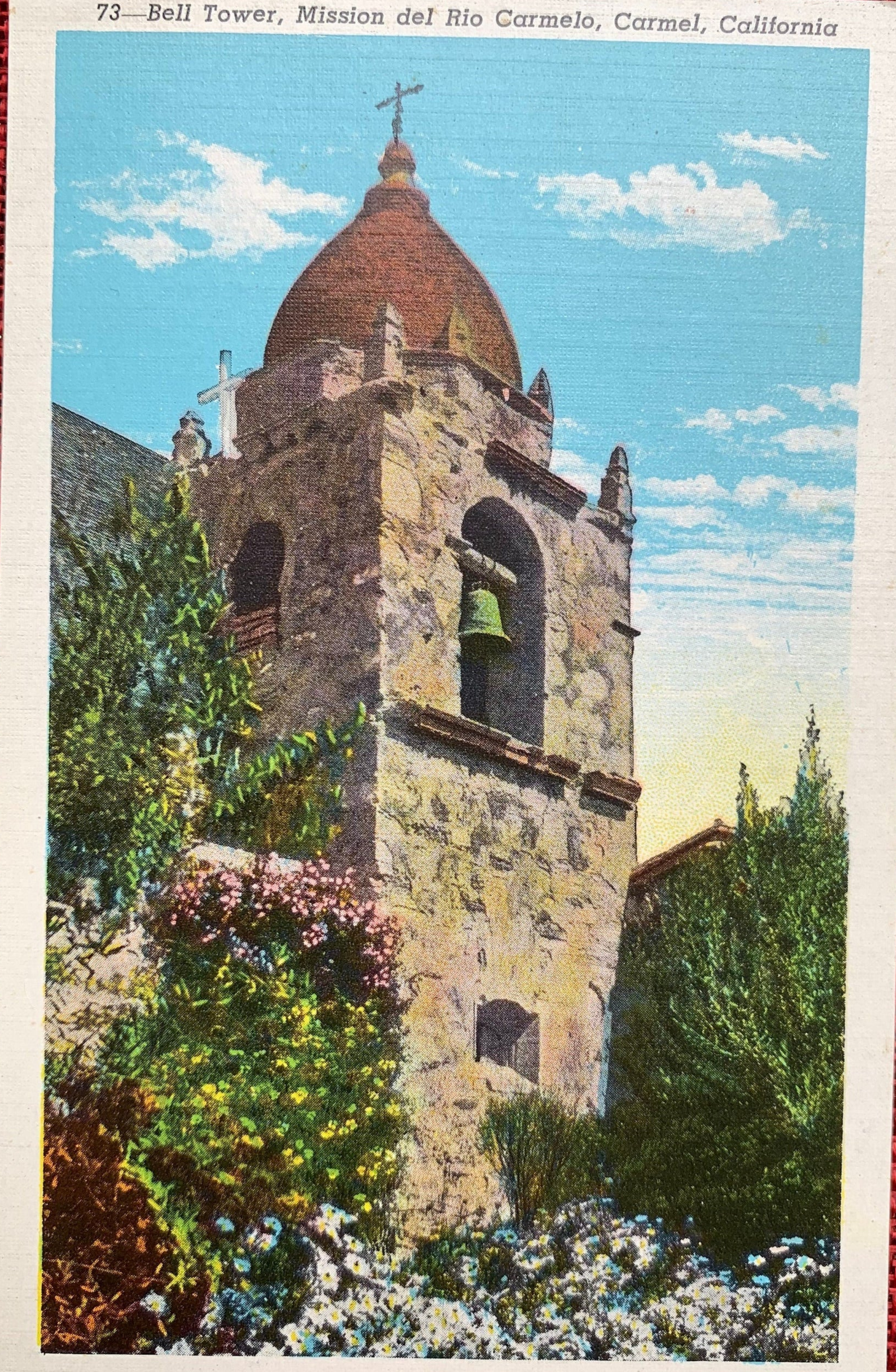 Bell tower of Mission del Río Carmelo with trees and flowers in the foreground