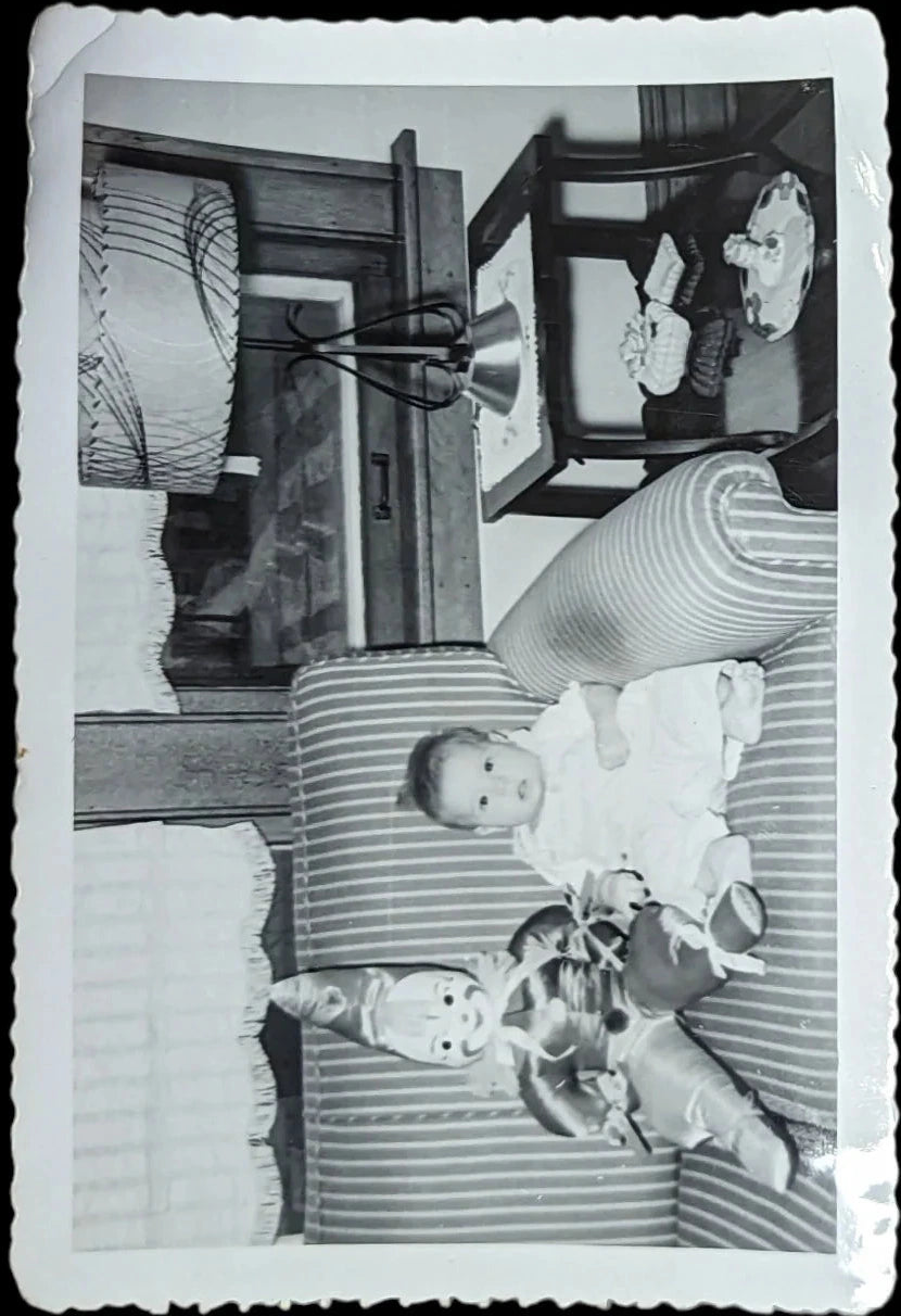 Vintage black and white photo of a baby with a toy clown on a striped couch