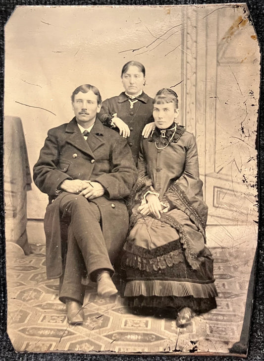 Vintage black and white photograph of a family sitting together, with a patterned floor and wall in the background.