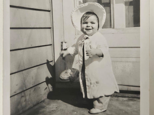 Baby Girl In White Outfit with Sun Bonnet- Holding a large Top Smiling - Spring Baby Photo - Black and White Photograph 1950s