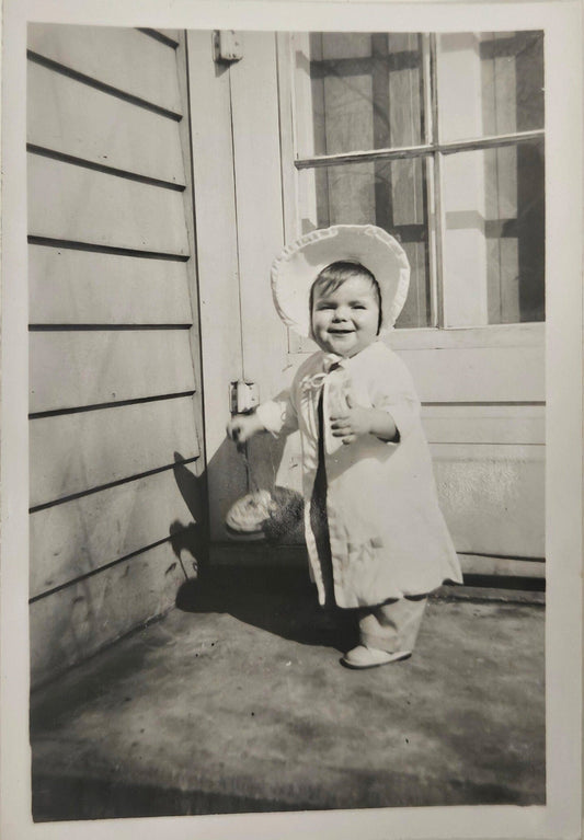 Baby Girl In White Outfit with Sun Bonnet- Holding a large Top Smiling - Spring Baby Photo - Black and White Photograph 1950s