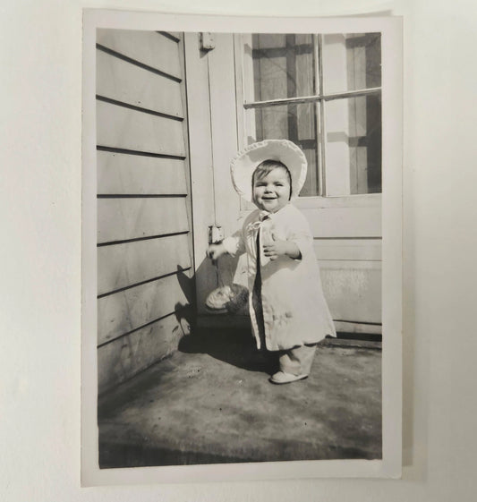 Baby Girl In White Outfit with Sun Bonnet - Holding a large Top Smiling - Spring Baby Photo - Black and White Photograph 1950s