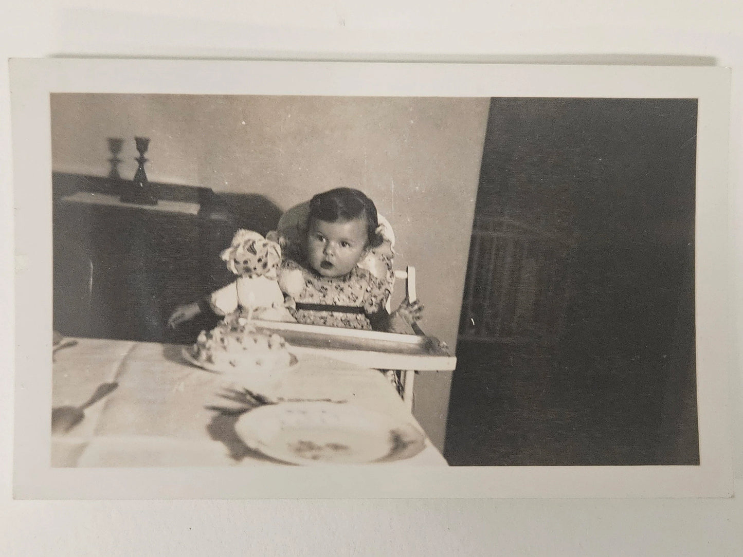 Photograph of Baby's First Birthday  - Late 1930s Real Photograph - Baby Girl in Highchair with Doll and Cake with one candle - Black and White Photo