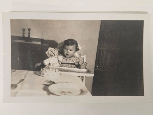 Photograph of Baby's First Birthday  - Late 1930s Real Photograph - Baby Girl in Highchair with Doll and Cake with one candle - Black and White Photo