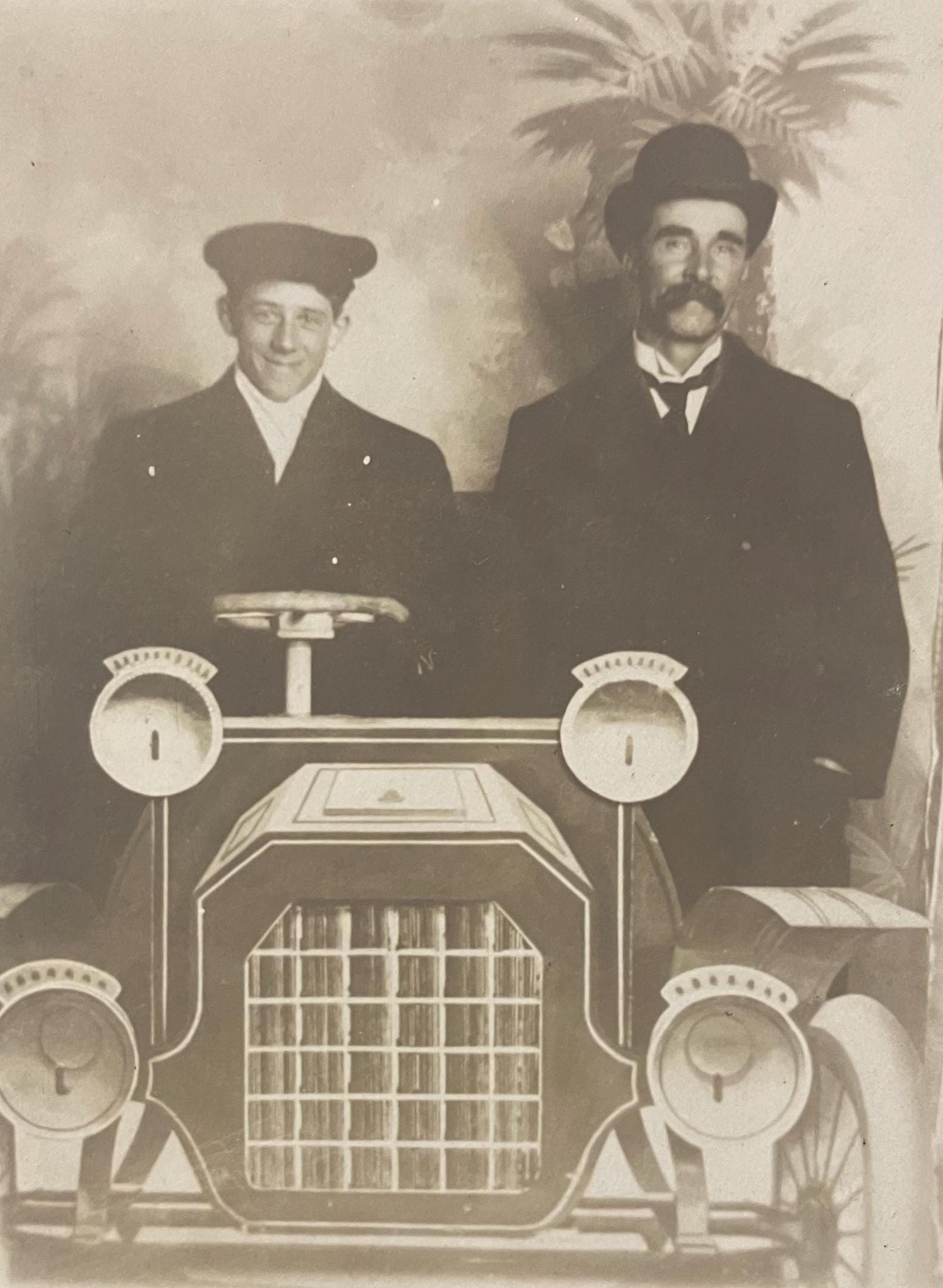 A black and white photo of two men posing with a prop car designed for a photograph, likely a parody image.