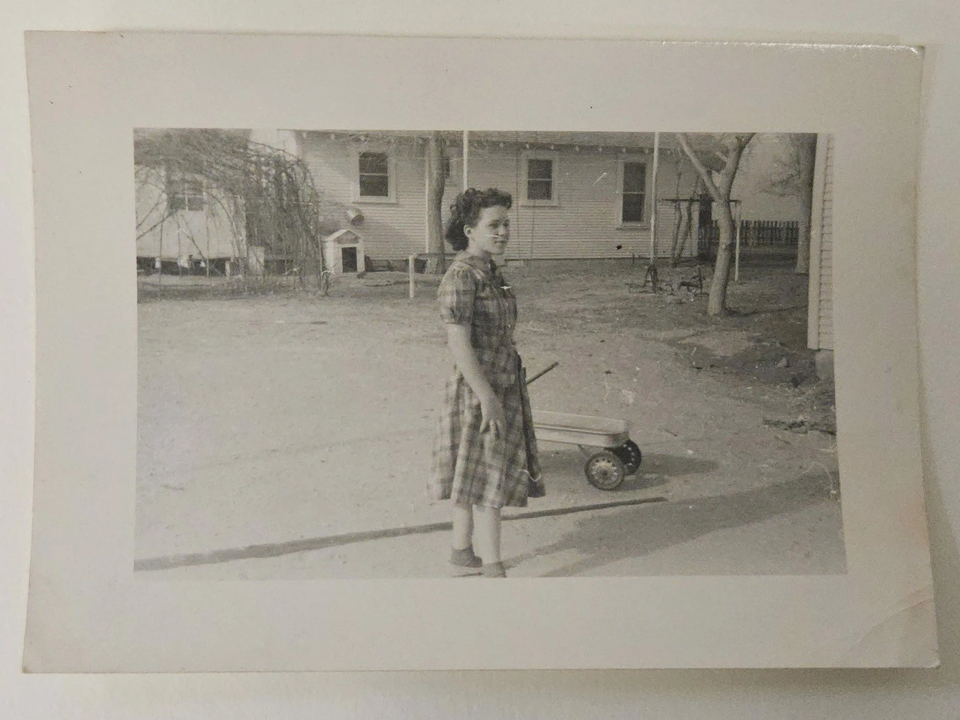 Vintage black and white photo of a woman standing next to a child's wagon in a yard.