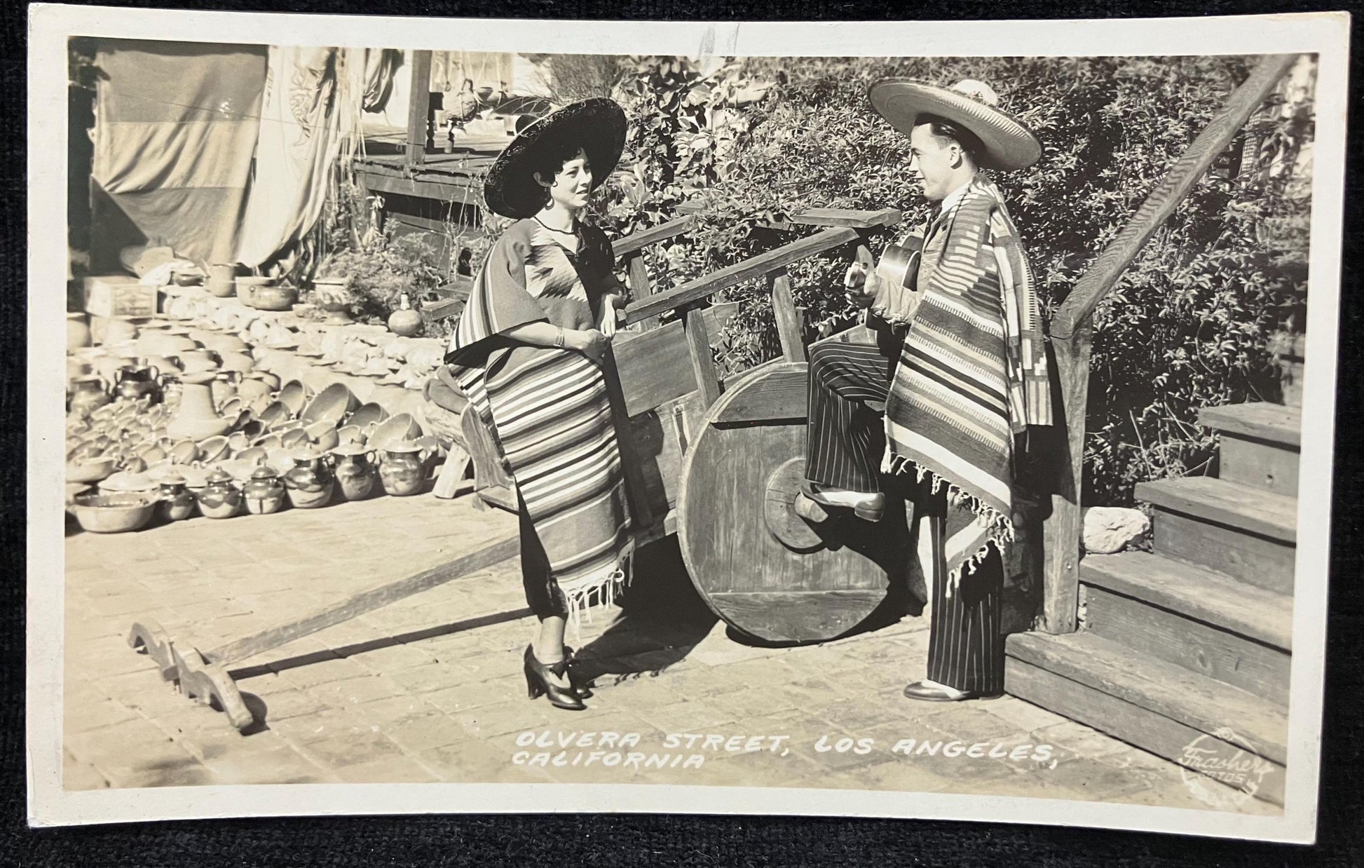 Vintage black and white photo of a couple on a wooden deck with a scenic background in Olvera Street, Los Angeles, Calif.