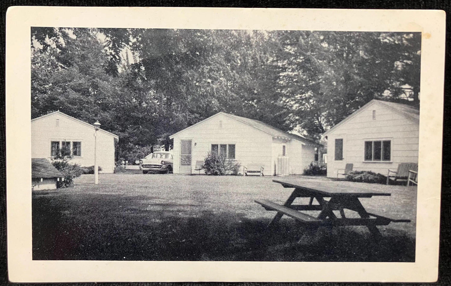 Vintage black and white photo of a row of small houses with a picnic table in a yard.