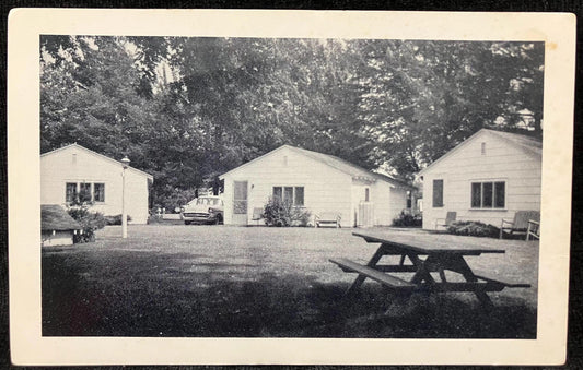 Vintage black and white photo of a row of small houses with a picnic table in a yard.