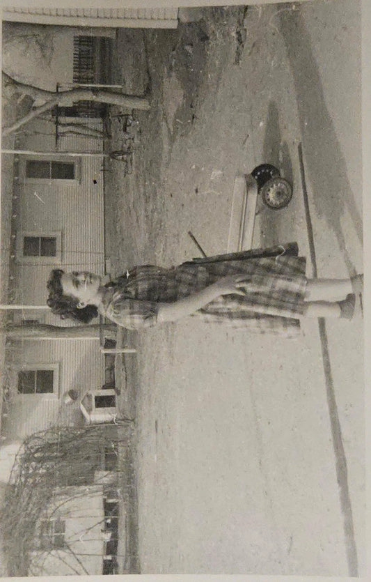Vintage black and white photo of a person standing outdoors with a house in the background