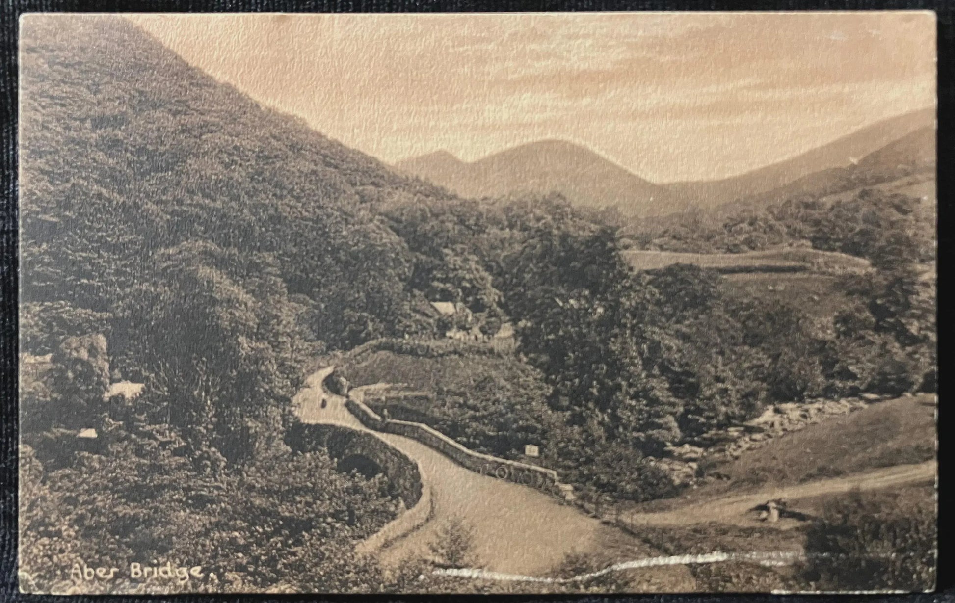Vintage sepia-toned photograph of a winding road through a forested valley.