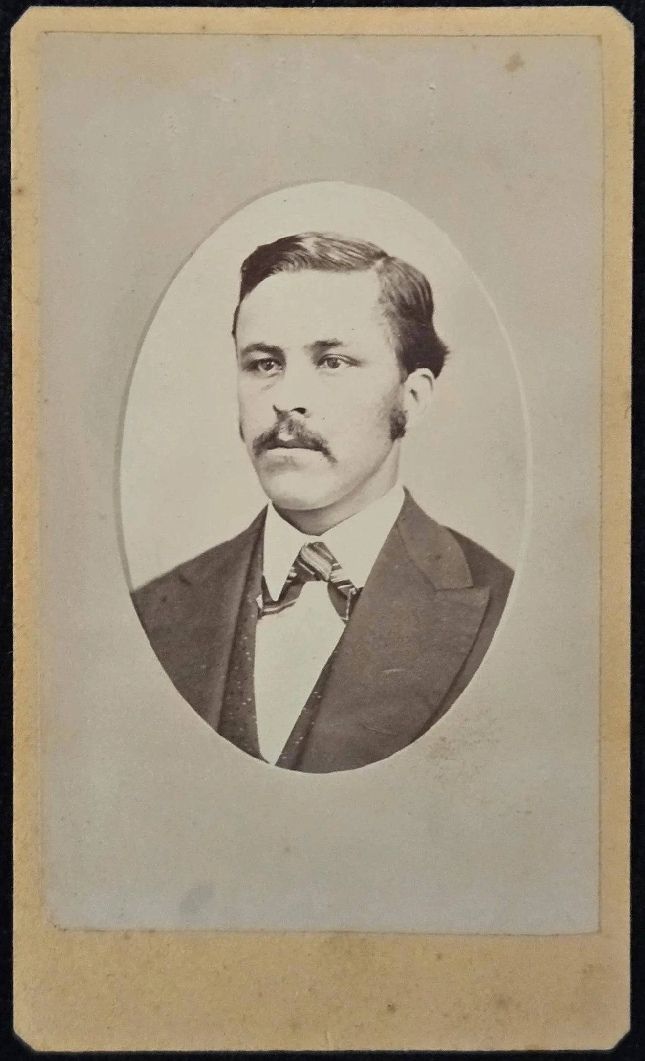 Vintage portrait of a man with a mustache in formal attire, framed in an oval on a beige background.
