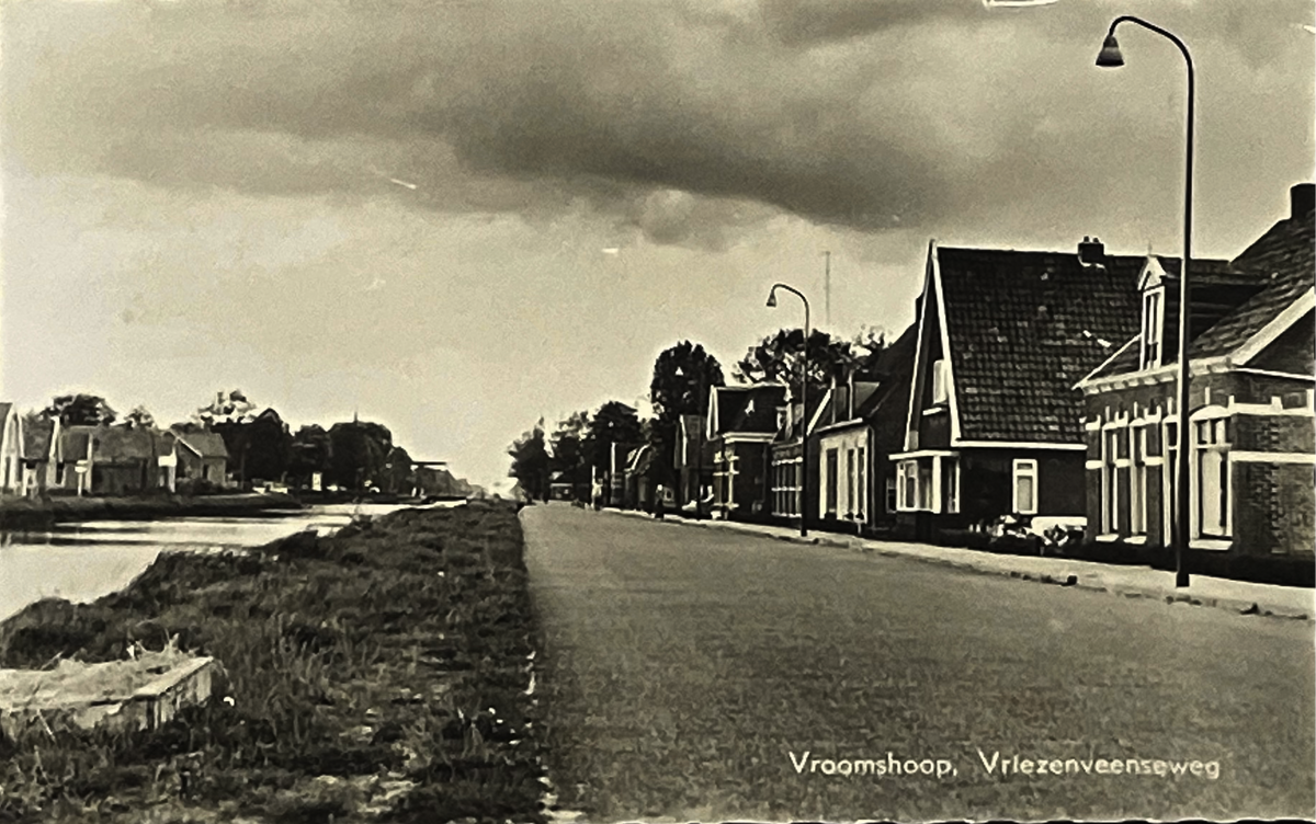 Vintage black and white photo of a Dutch canal scene with buildings and trees in Vroomshoop, Netherlands. 