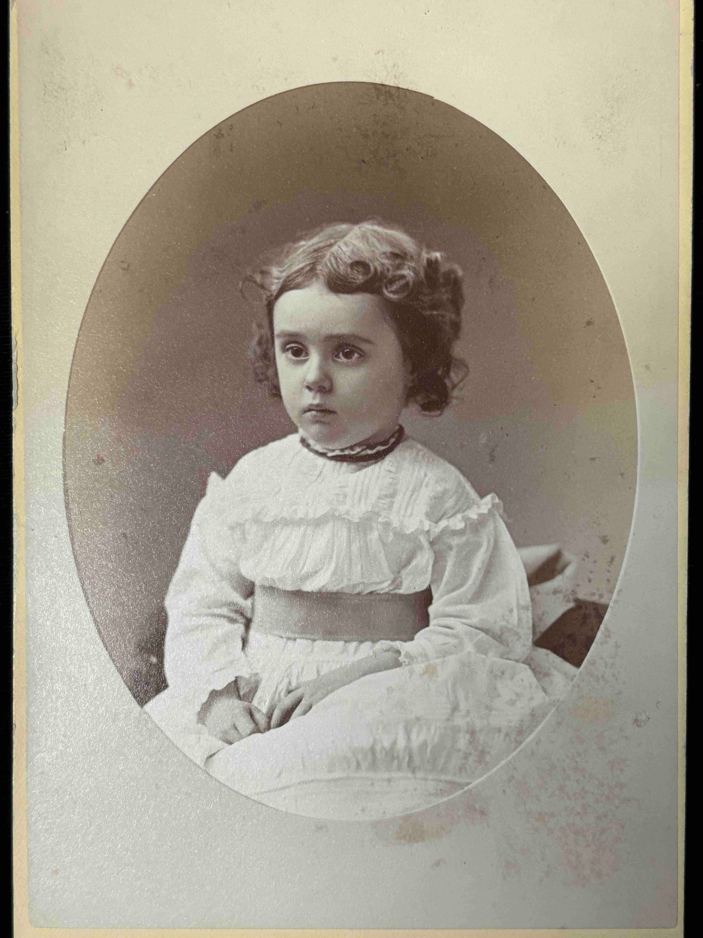 Vintage photograph of a young girl in a white dress with ruffled collar.