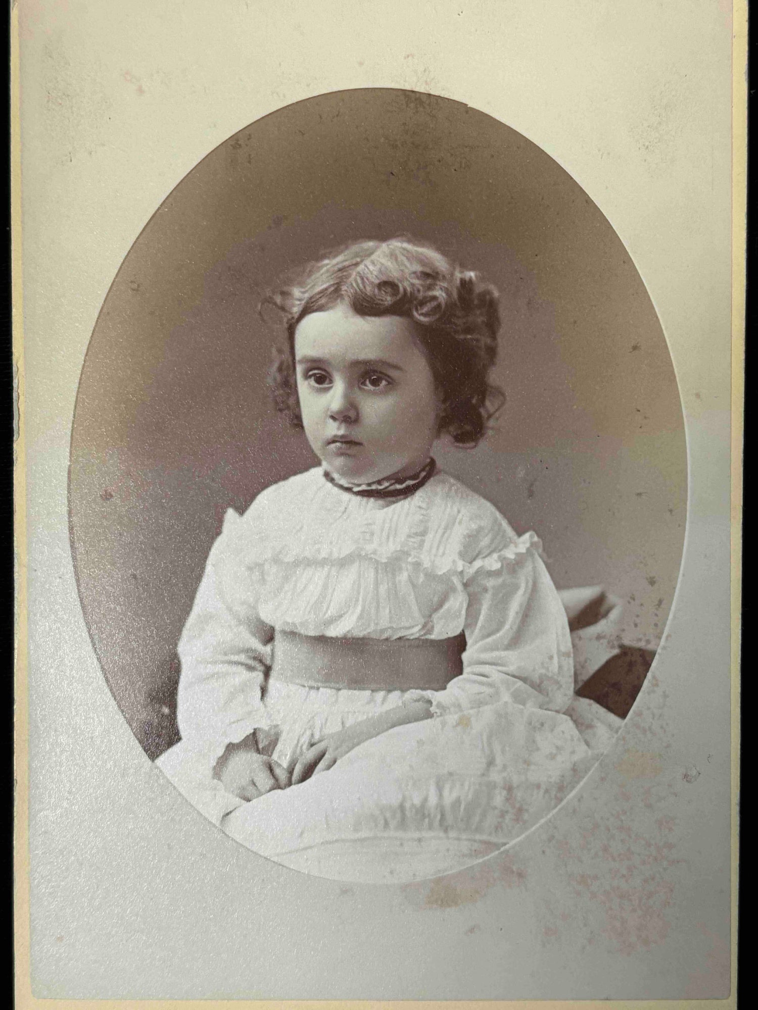 Vintage photograph of a young girl in a white dress with ruffled collar.