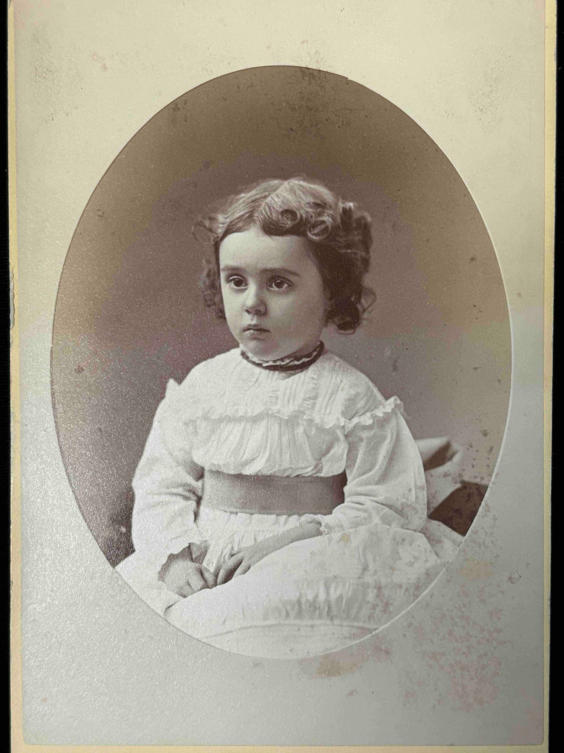 Vintage photograph of a young girl in a white dress with ruffled collar.