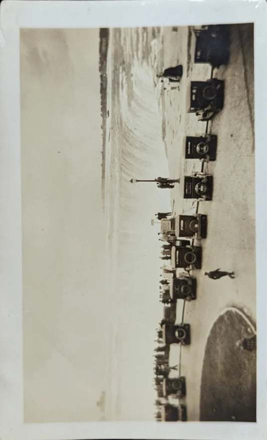 Vintage black and white photo of a man walking near a waterfall with a dog, surrounded by multiple cars.